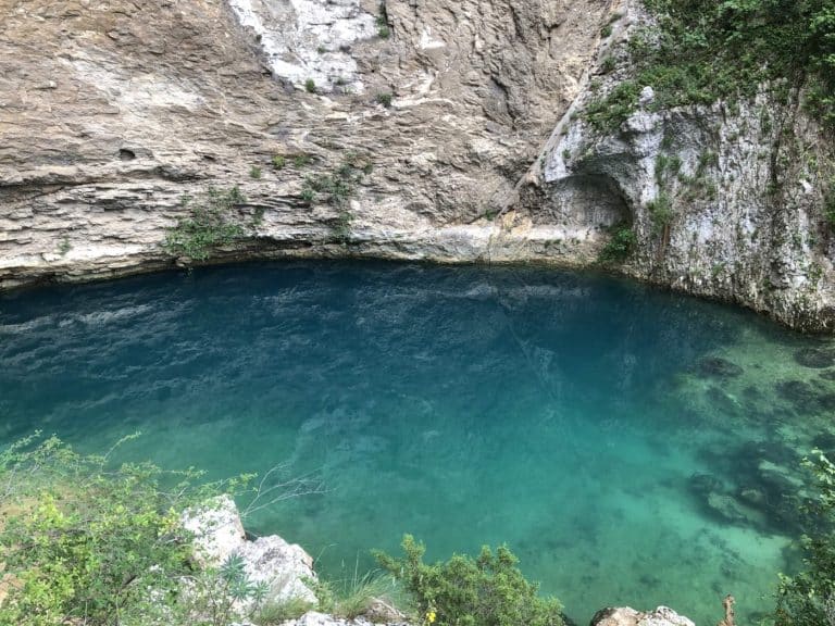 The turquoise waters of the Fontaine-de-Vaucluse chasm at the foot of the cliff