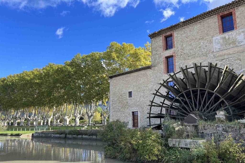 The Moulin Saint-Pierre des Taillades and its large waterwheel by the canal, beneath the autumn-coloured plane trees